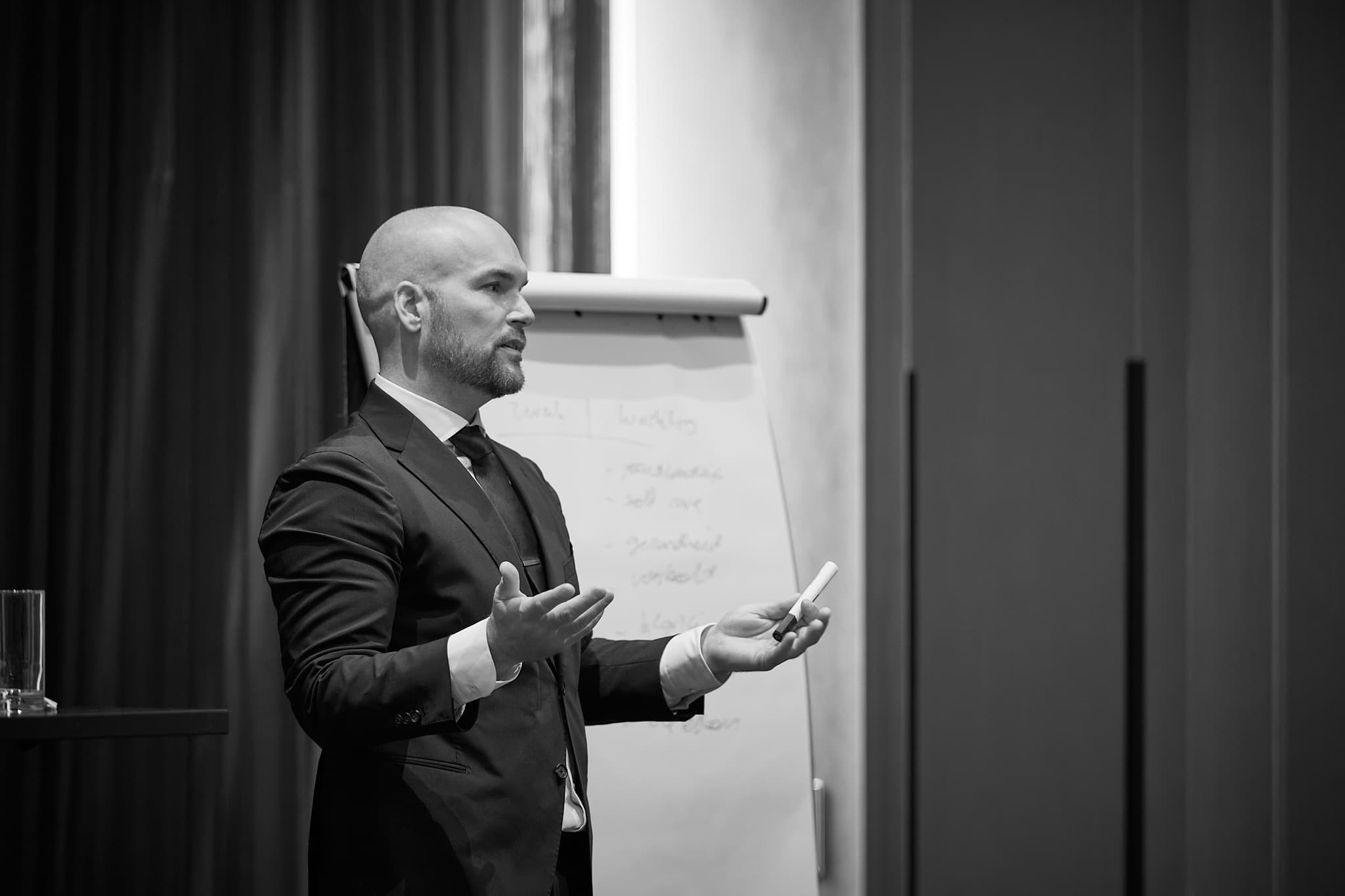Nick gebaart sprekend voor de groep, zwart-wit